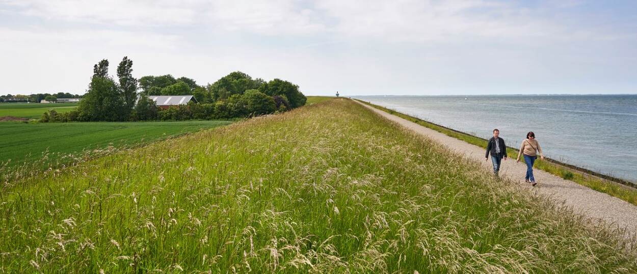 Twee wandelende mensen tussen weiland en water