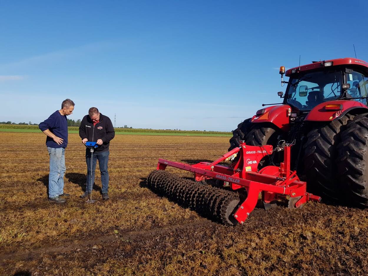 2 mannen met bodemmeetapparaat en rood grondwerk voertuig