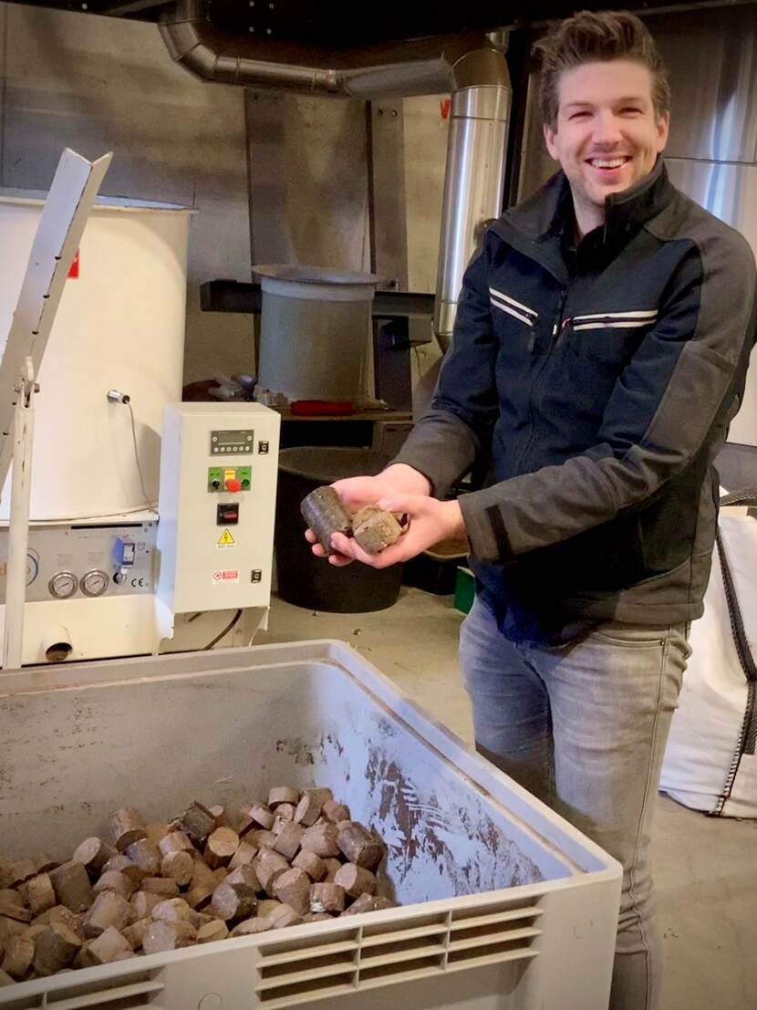 Man naast grote bak briketten met briketten in de hand