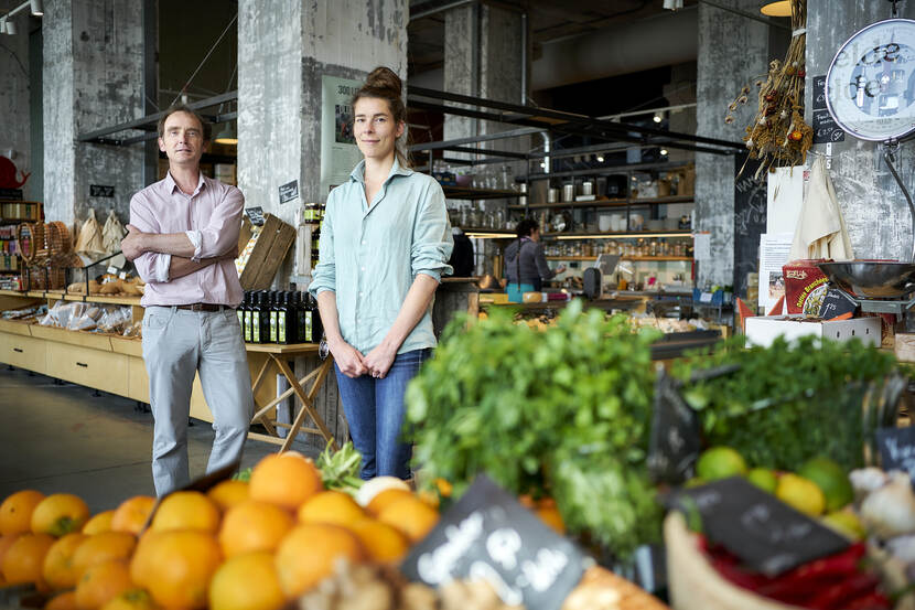 Man en vrouw voor toonbank in winkel met groente en fruit op de voorgrond