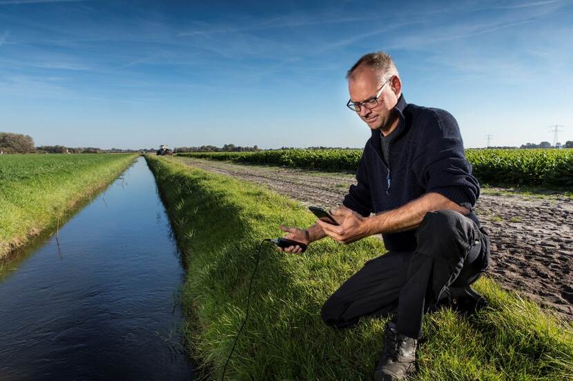 man in grasrand aan slootkant met meetapparatuur hangend in het water