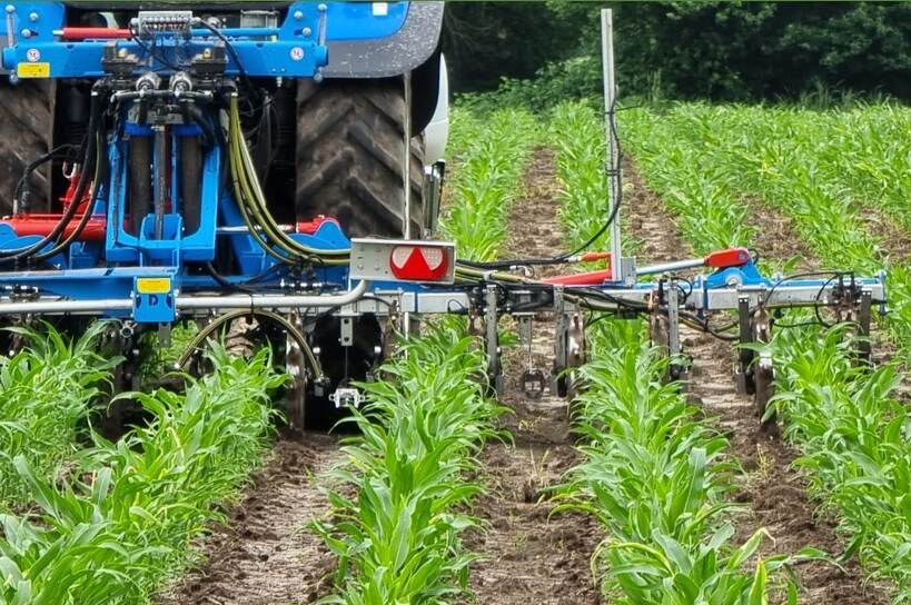 blauw landbouwvoertuig wat over het land rijdt en precisiebemesting uitvoert