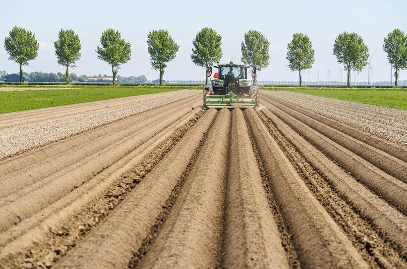 Groen landbouwvoertuig wat strepen trekt in de bruine landbouwgrond